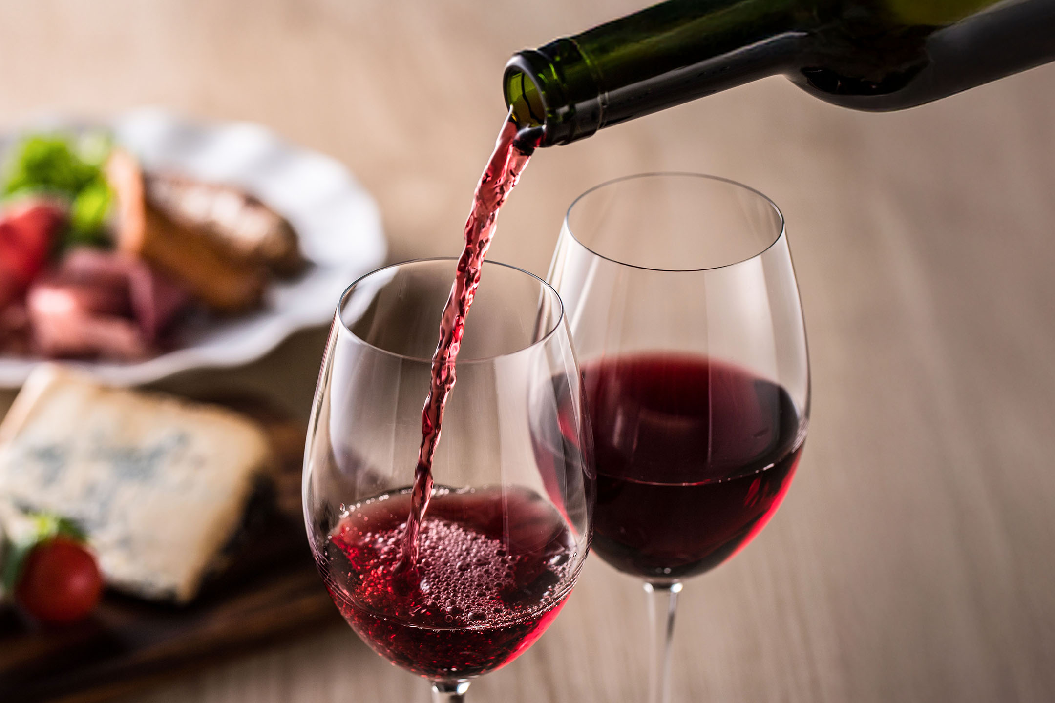 Rødvin hældes i et glas, med forretter i baggrunden.