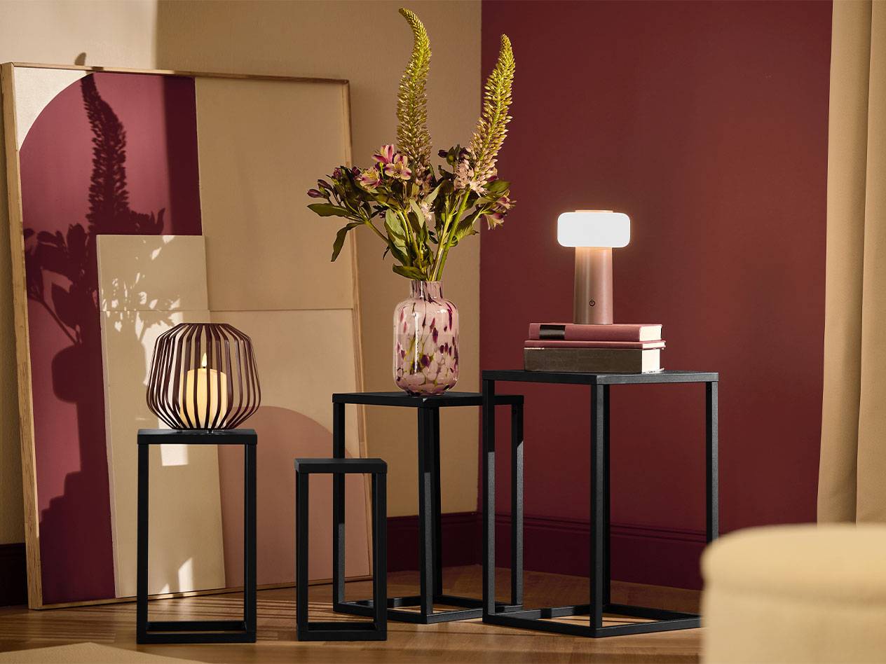 Tre sorte sideborde med et stearinlys, en vase med blomster og en lampe.