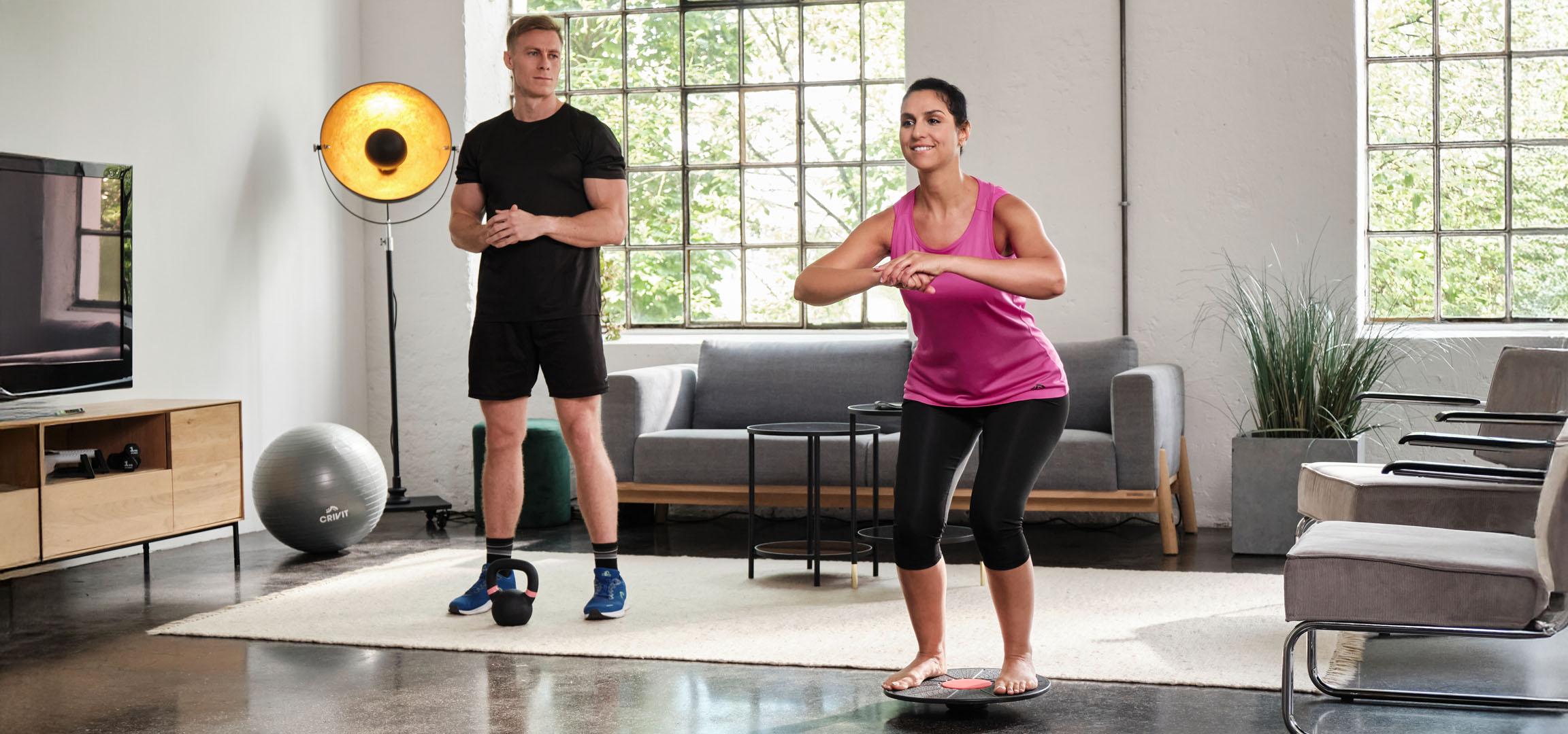 Kvinde og mand træner hjemme med balancebræt og kettlebell.