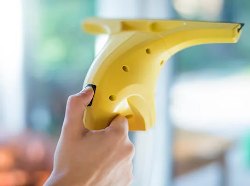 Hånd holder en gul elektrisk vinduesrenser, der rengør et vindue.