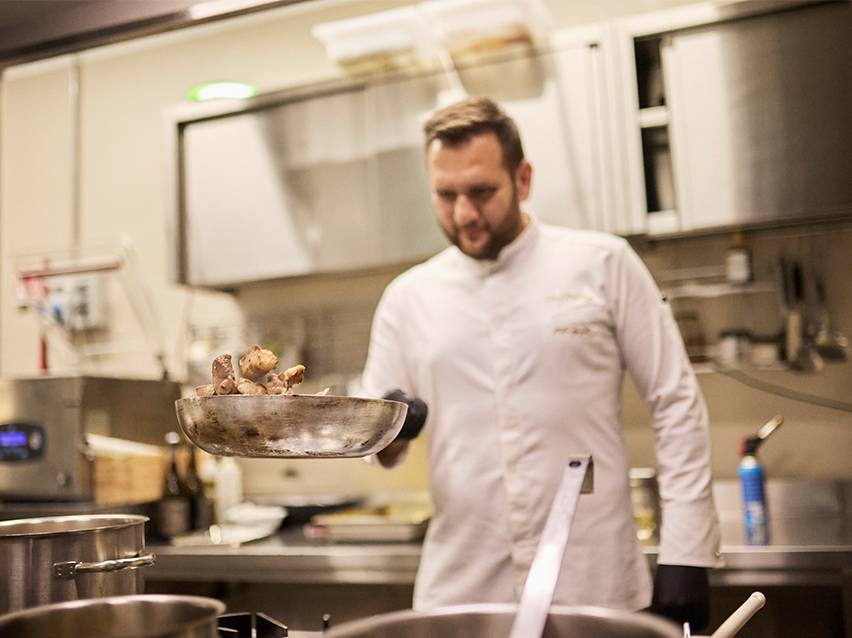 En kok i hvid kokkejakke kaster mad i en pande.