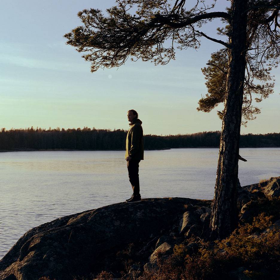 Mand i vandrejakke ved en sø, med et træ i forgrunden.