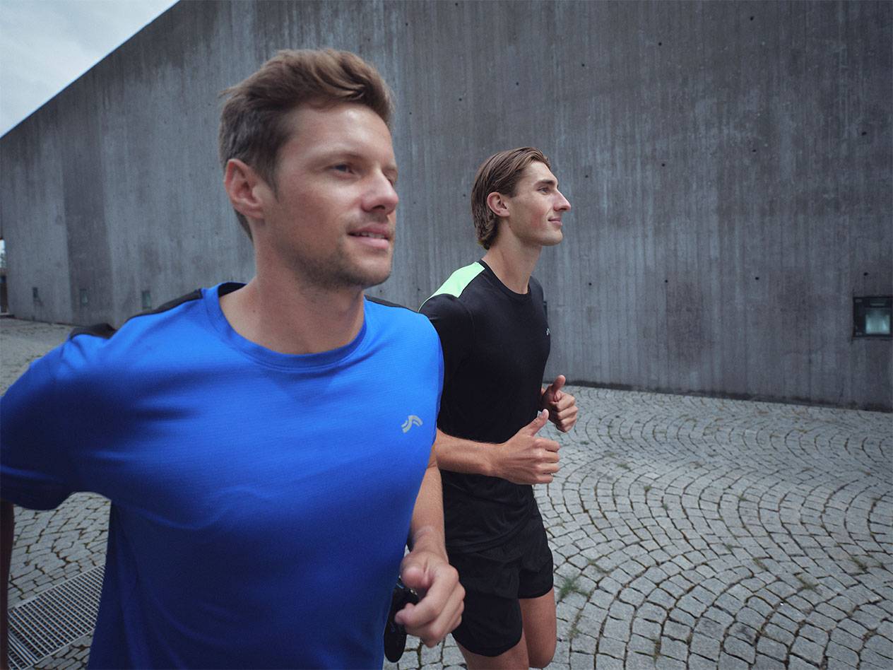 To mænd løber i sportst-shirts og shorts, en blå og en sort.