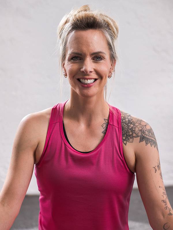 En smilende kvinde i en pink sportstop med skuldertatoveringer.