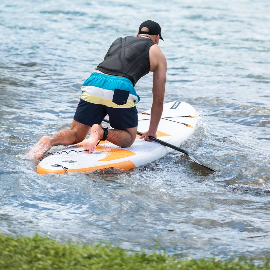 Mand knælende på et paddleboard med pagaj i vandet.