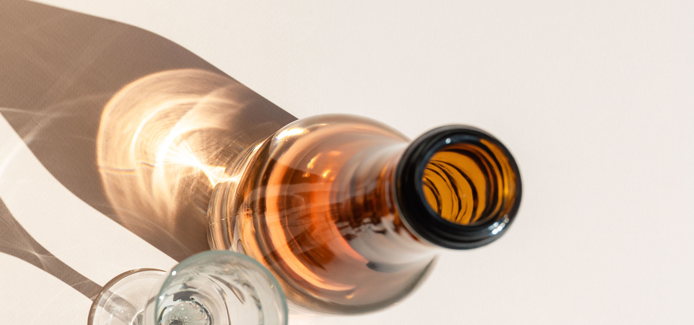 Glas og flaske med skygger og lysrefleksioner på en lys baggrund