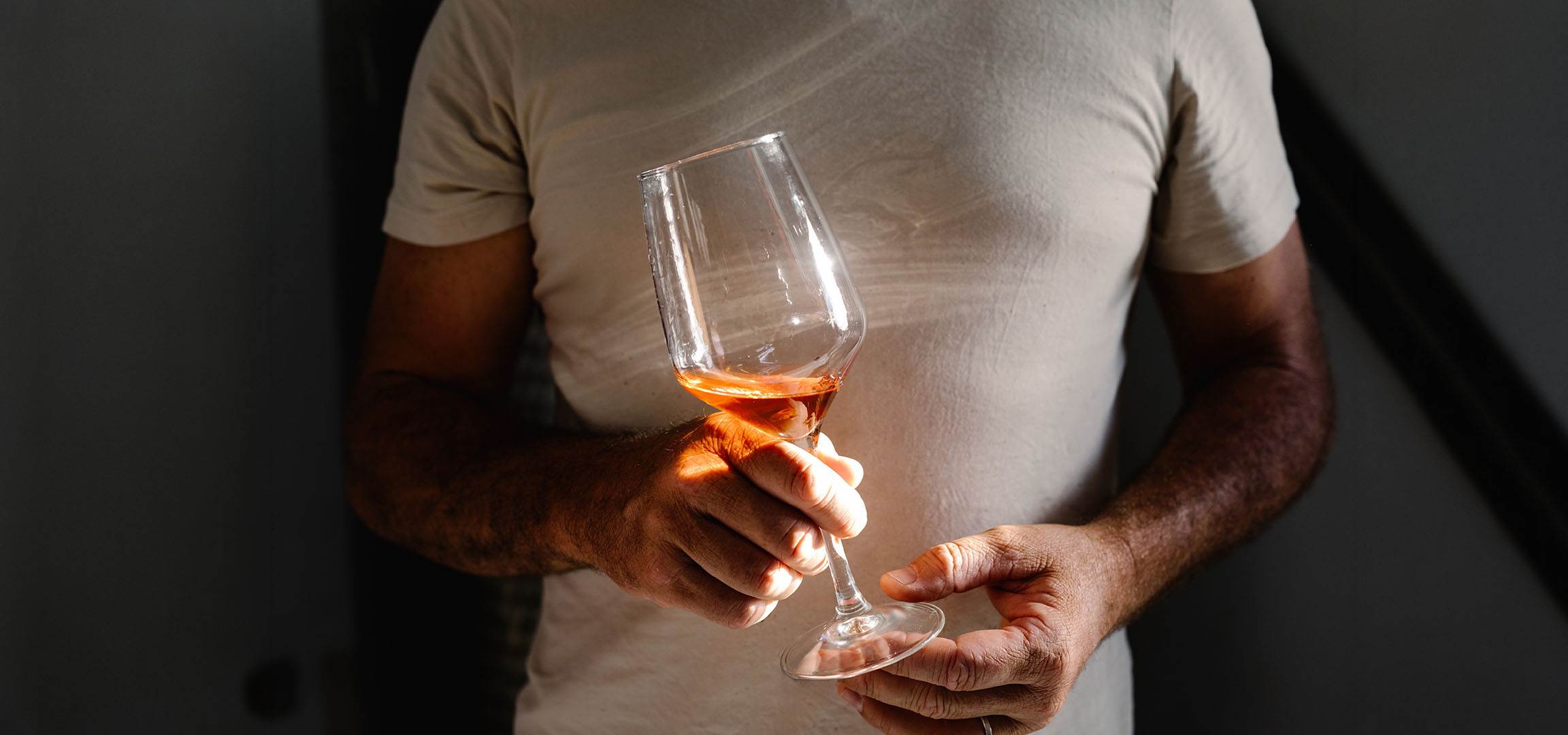Mand holder et glas rosévin, badet i sollys, mod en mørk baggrund.