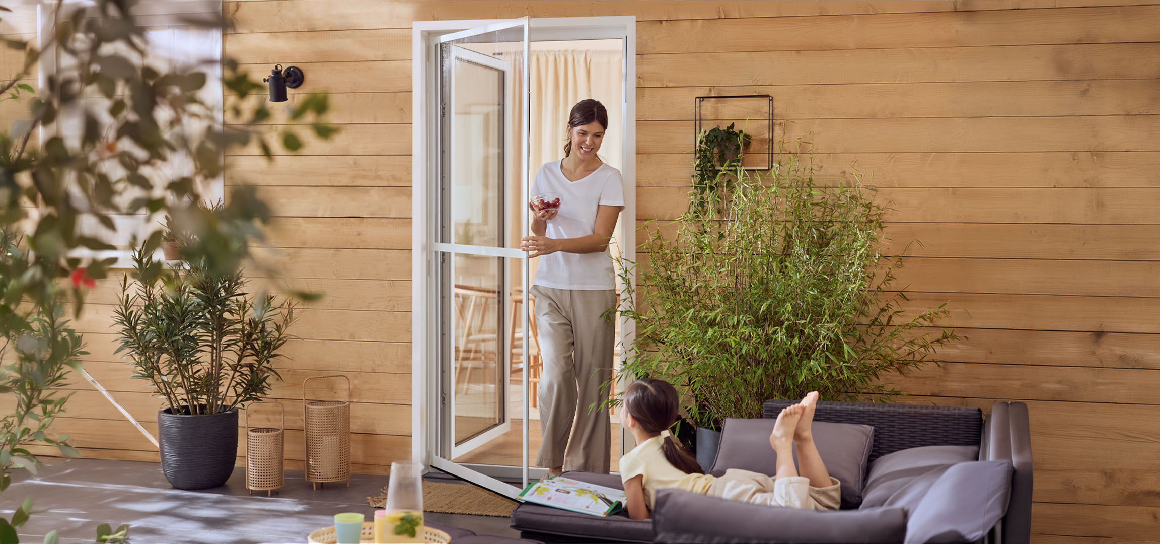 Kvinde og pige nyder terrassen med udendørsmøbler og planter.