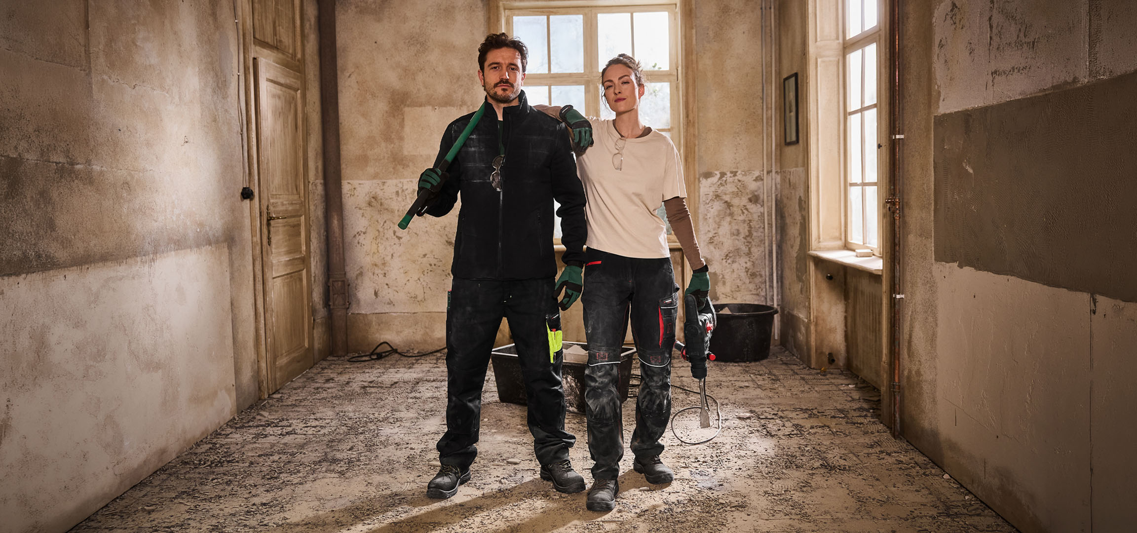 To bygningsarbejdere i arbejdstøj med værktøj på en byggeplads.