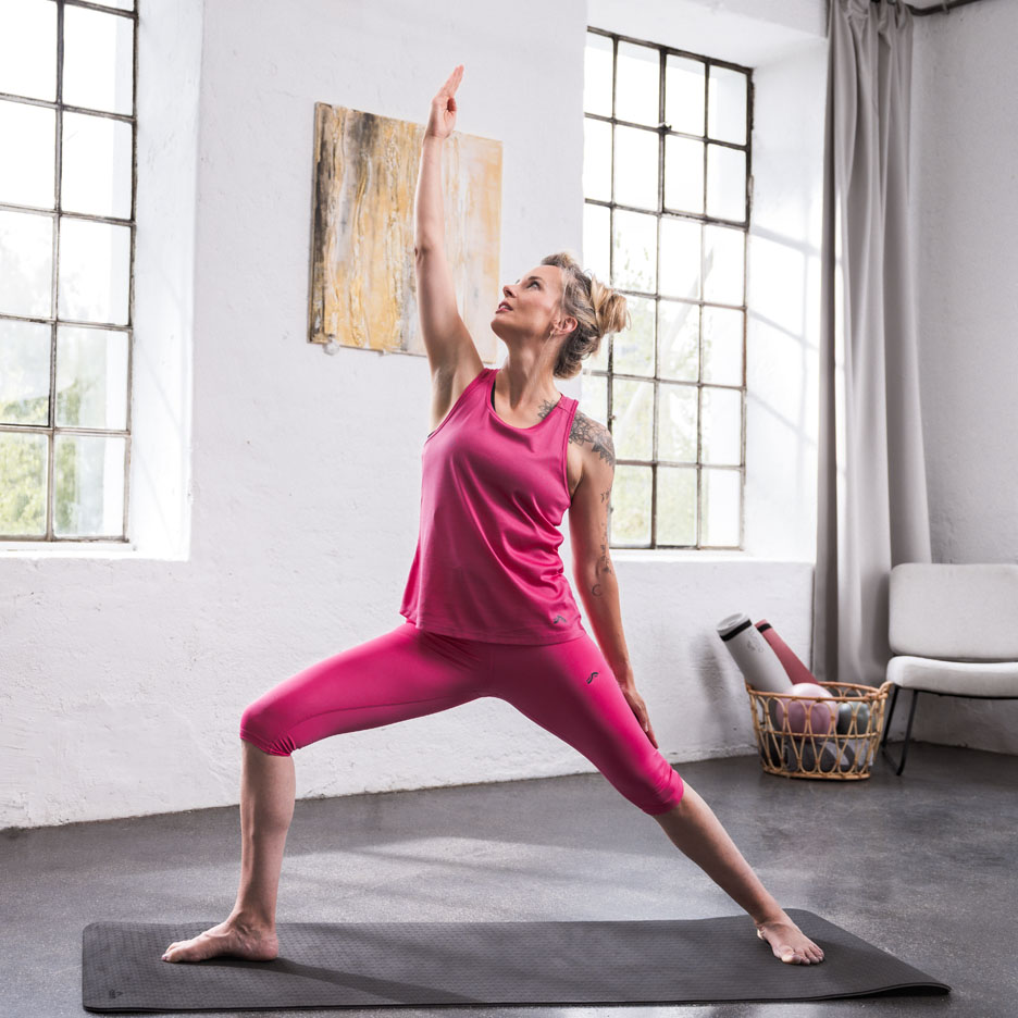 Kvinde laver yoga i lyserødt sportstøj i et lyst rum.