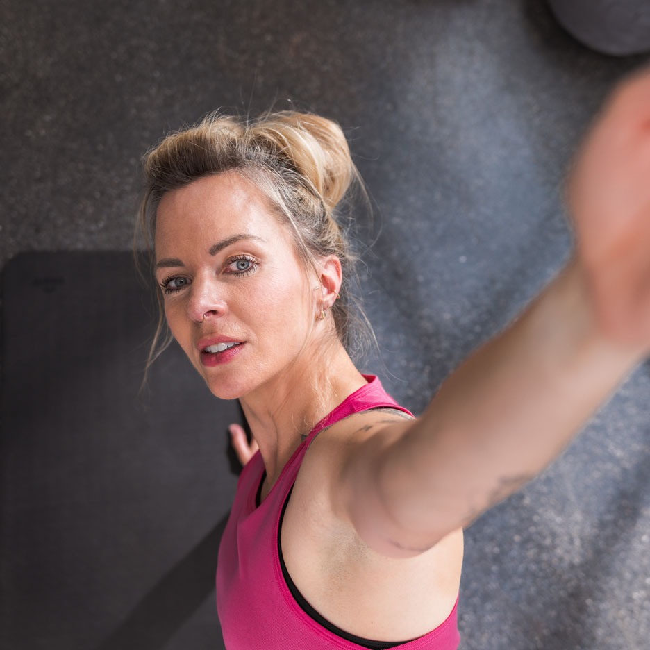 En kvinde i en pink sportstop tager en selfie i fitnesscentret.