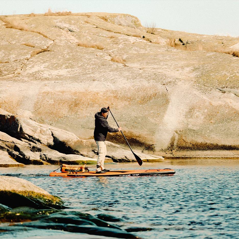 Mand padler på et orange paddleboard på en stenet sø.