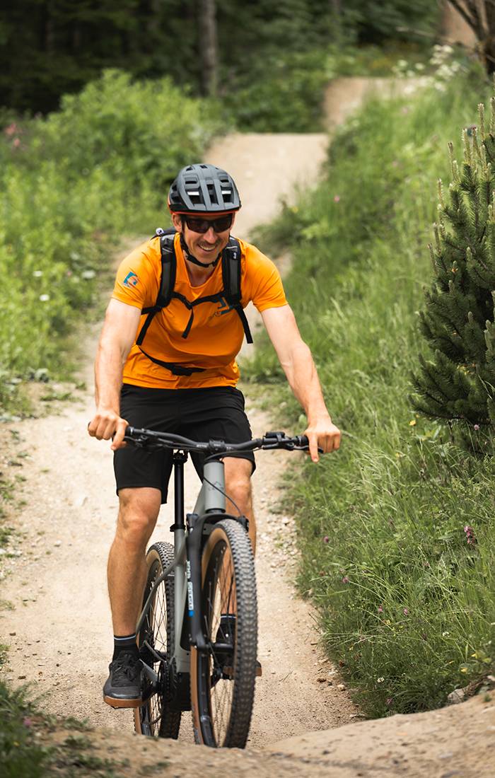 En mand smiler, mens han mountainbiker på en sti.