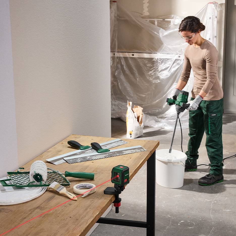 Kvinde blander byggemateriale med maler- og nivelleringsværktøj på et bord.