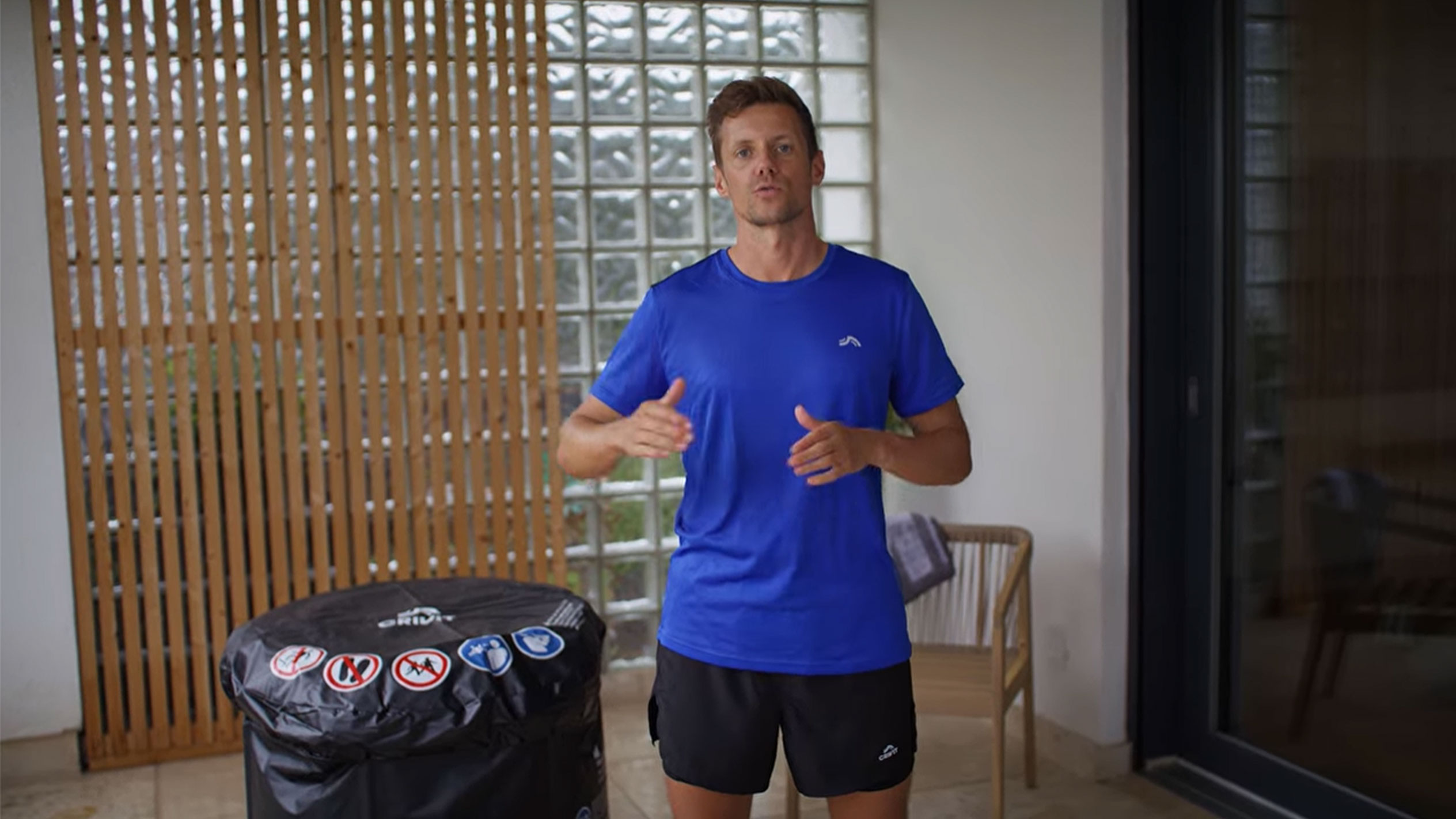 Mand i blå T-shirt og sorte shorts, ved siden af et sort spabadscover.