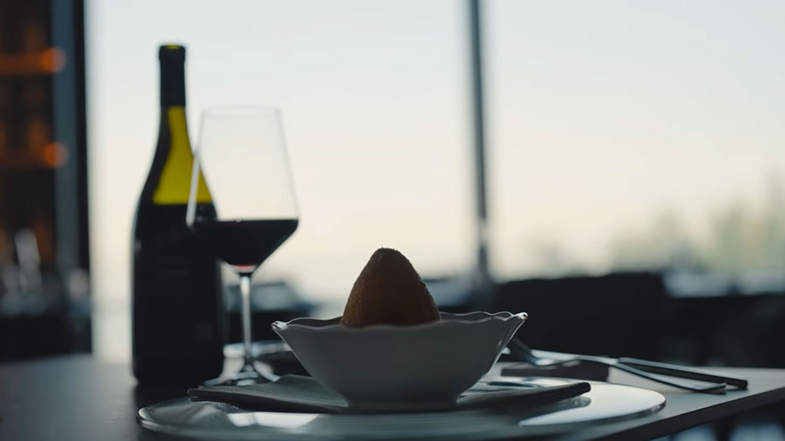 En flaske rødvin og et glas ved siden af en arancino i en skål på et bord.