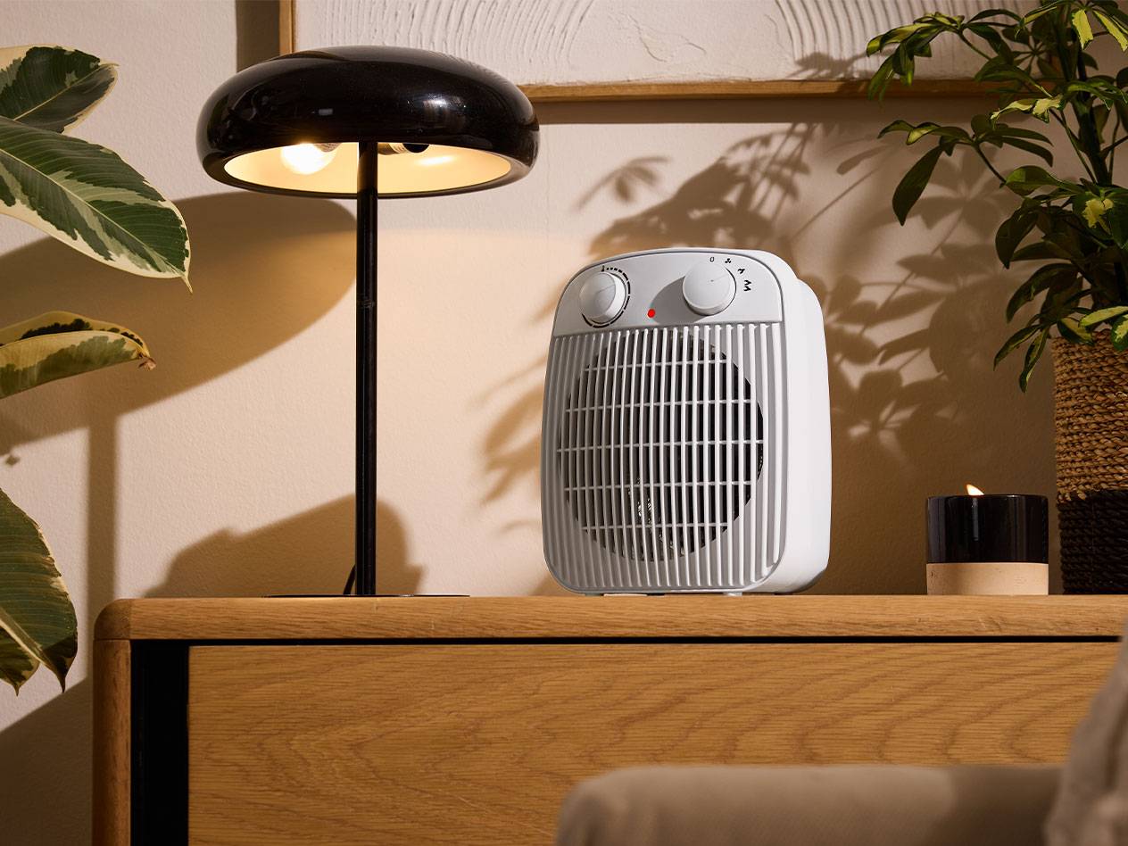 Hvid varmeblæser og sort bordlampe på et træmøbel i et hyggeligt rum.