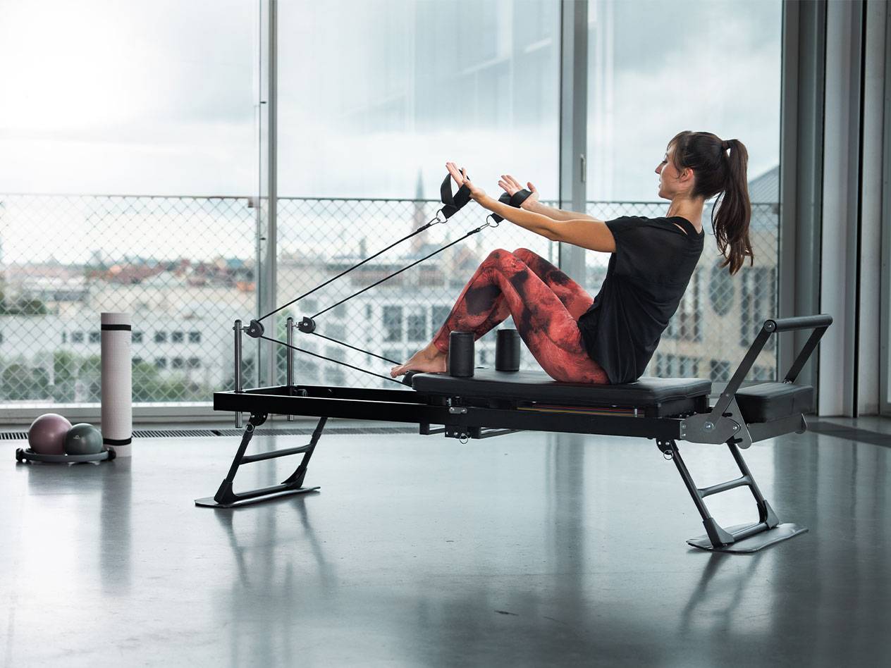 Kvinde dyrker pilates på en reformer med udsigt over byen.