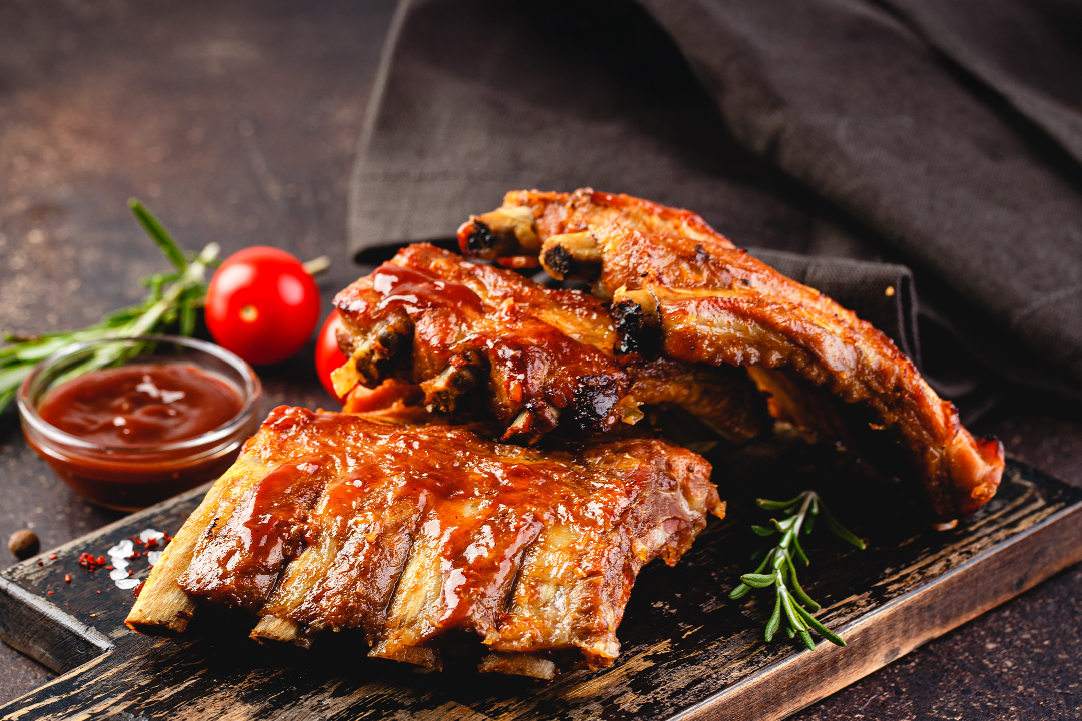 Grillede spareribs med barbecue sauce, rosmarin og tomater på et træskærebræt.