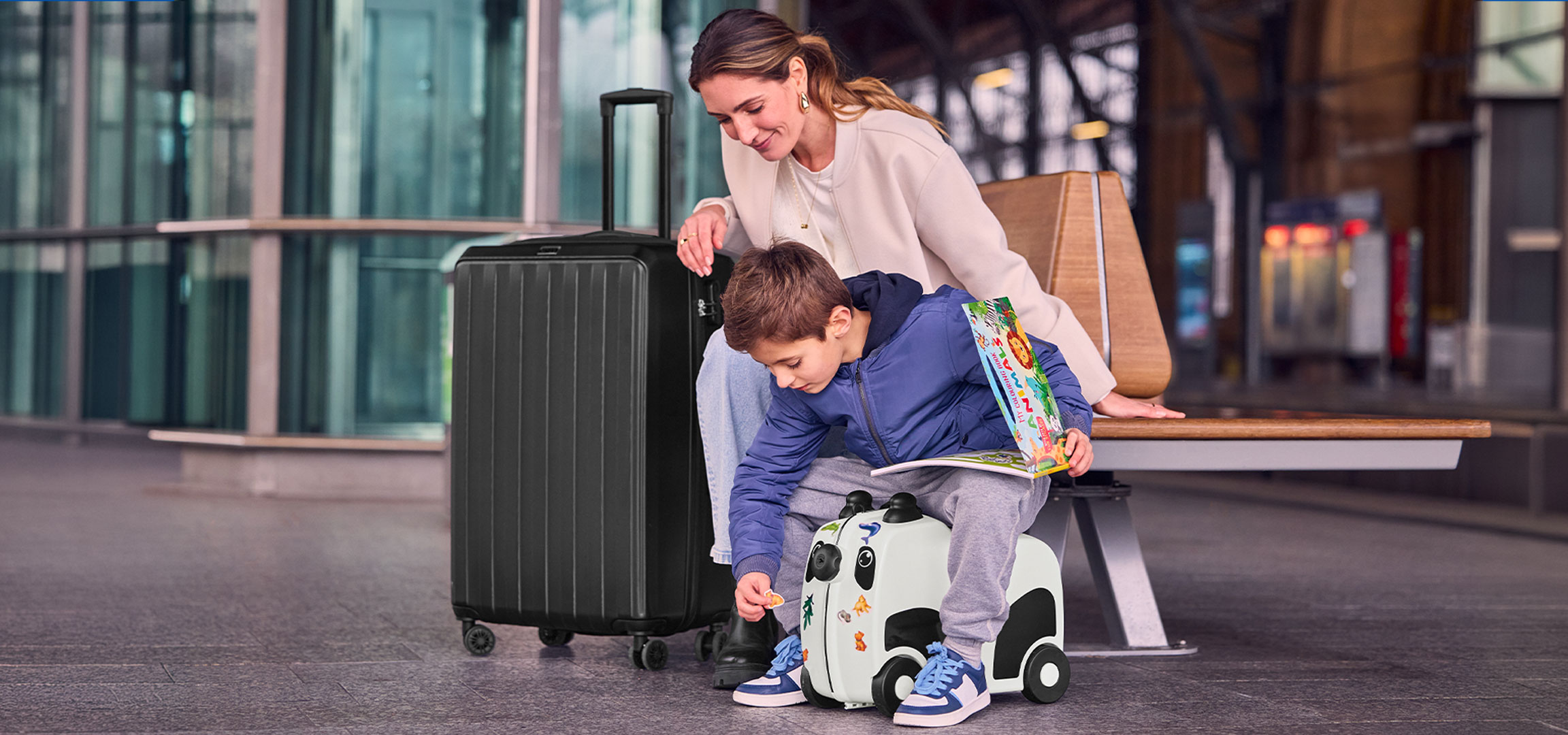 Mor og barn med bagage i lufthavnen, barnet leger med en kuffert med hjul.