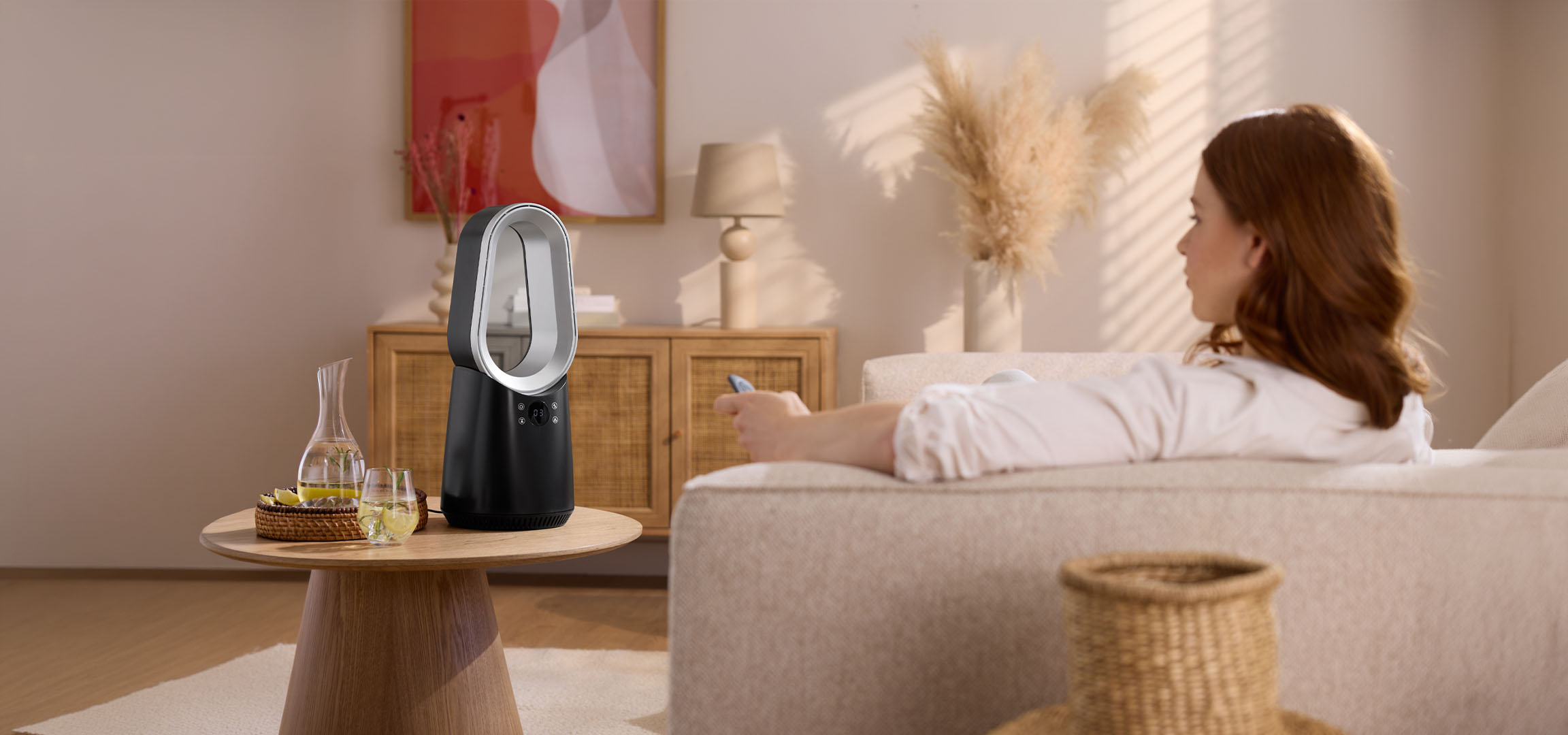 Kvinde på sofa med fjernbetjening, moderne ventilator og drikkevarer på bord.