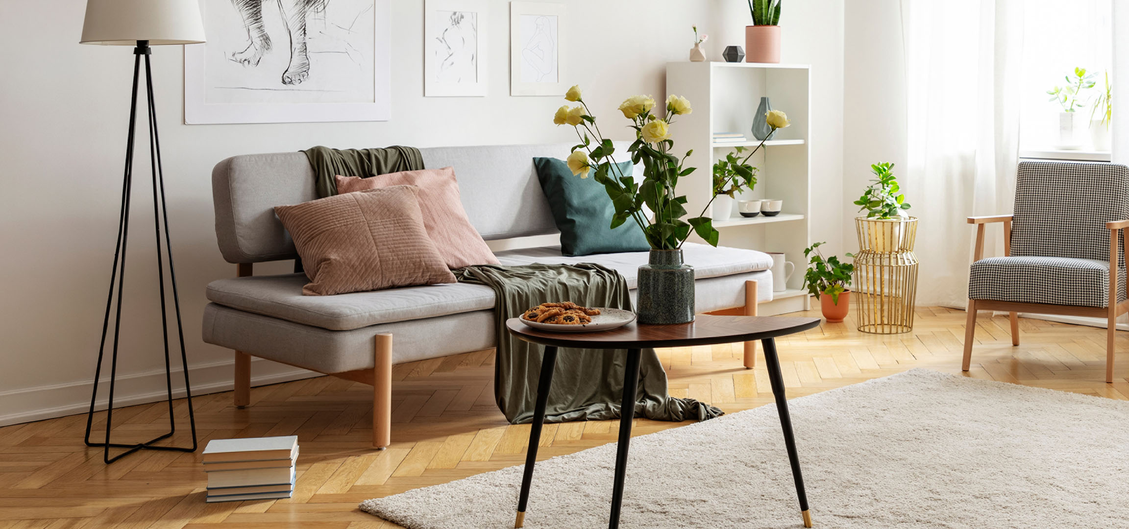 Hyggelig stue med grå sofa, puder, sofabord med småkager og en vase med blomster.
