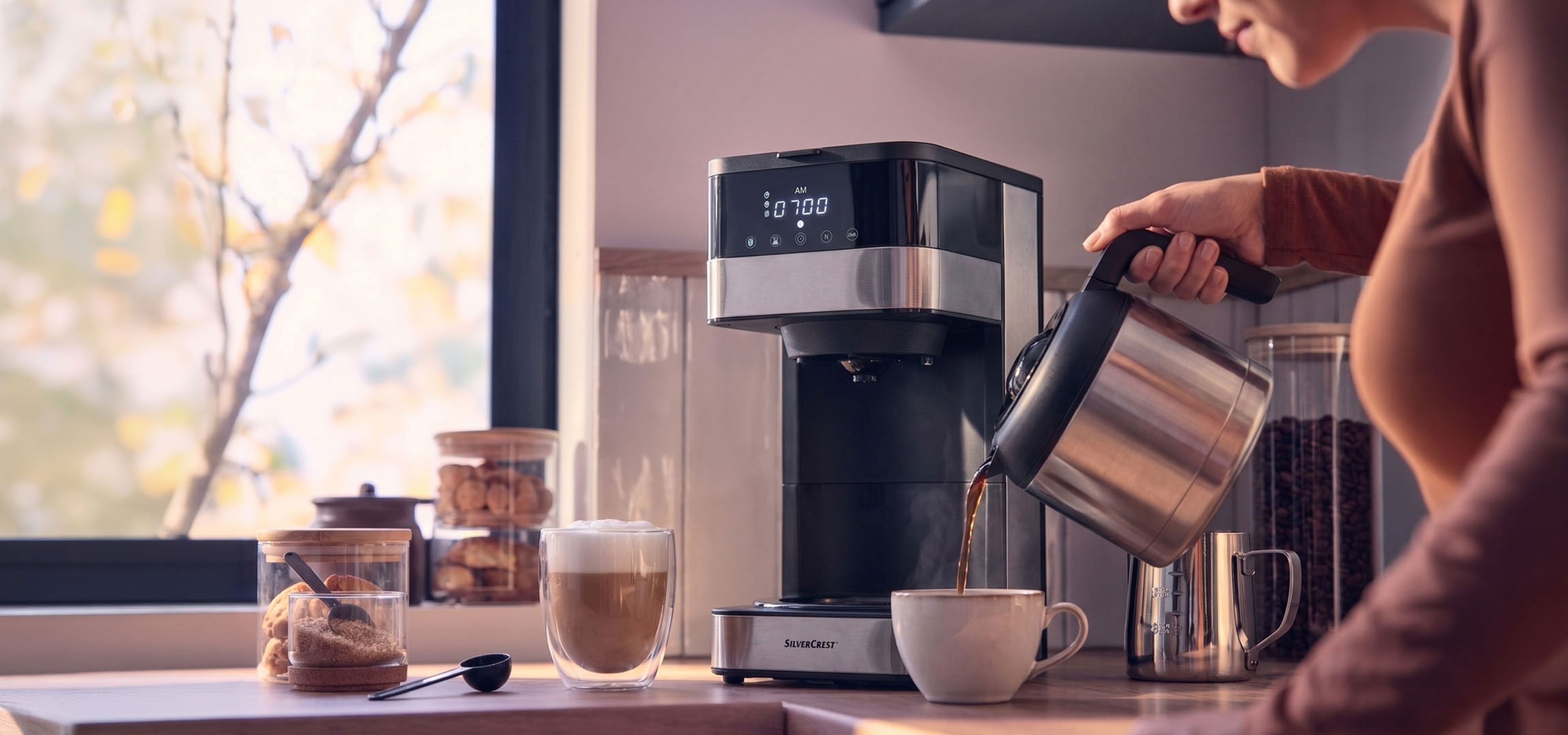 aiLabeling.aiLabelForImageAltText: Kaffemaskine skænker kaffe i en kop, med et lyst vindue i baggrunden.