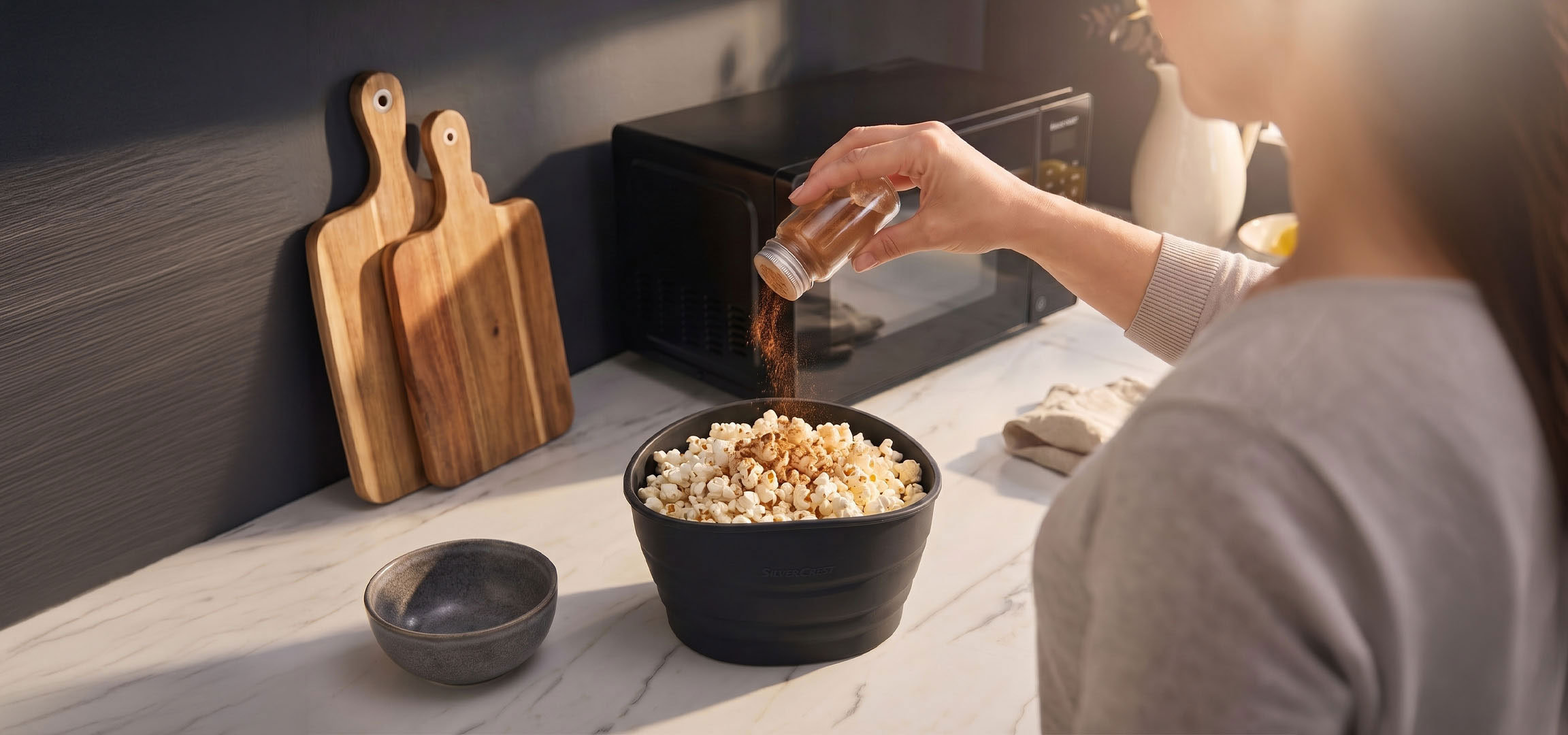 aiLabeling.aiLabelForImageAltText: Popcorn i en sort skål krydret med krydderier, ved siden af træskærebrætter.