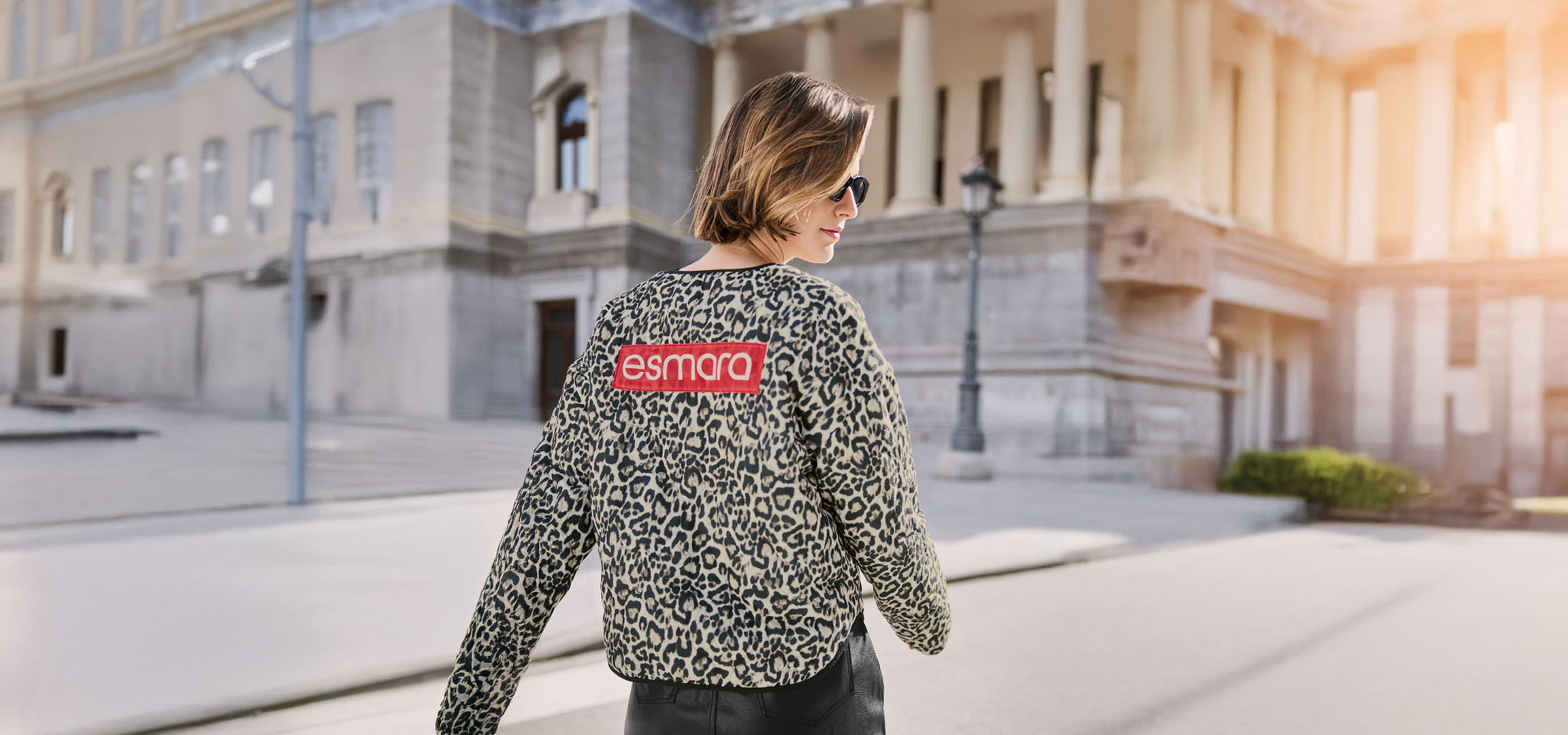 Kvinde i Esmara leopardjakke, solbriller, på en bygade.