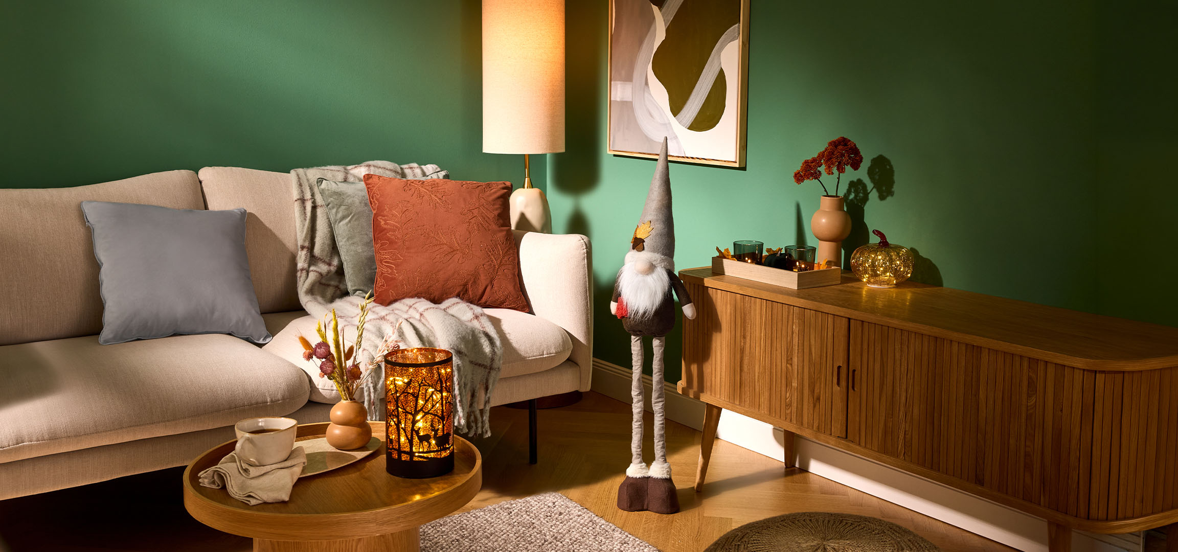 Hyggelig stue med beige sofa, puder, tæppe og efterårsdekorationer.