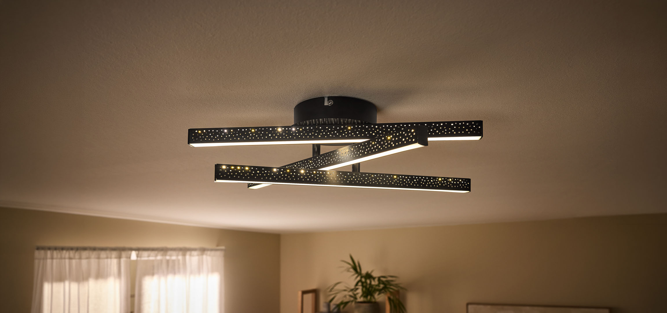Moderne LED-loftlampe med sorte, perforerede stænger og varmt lys.