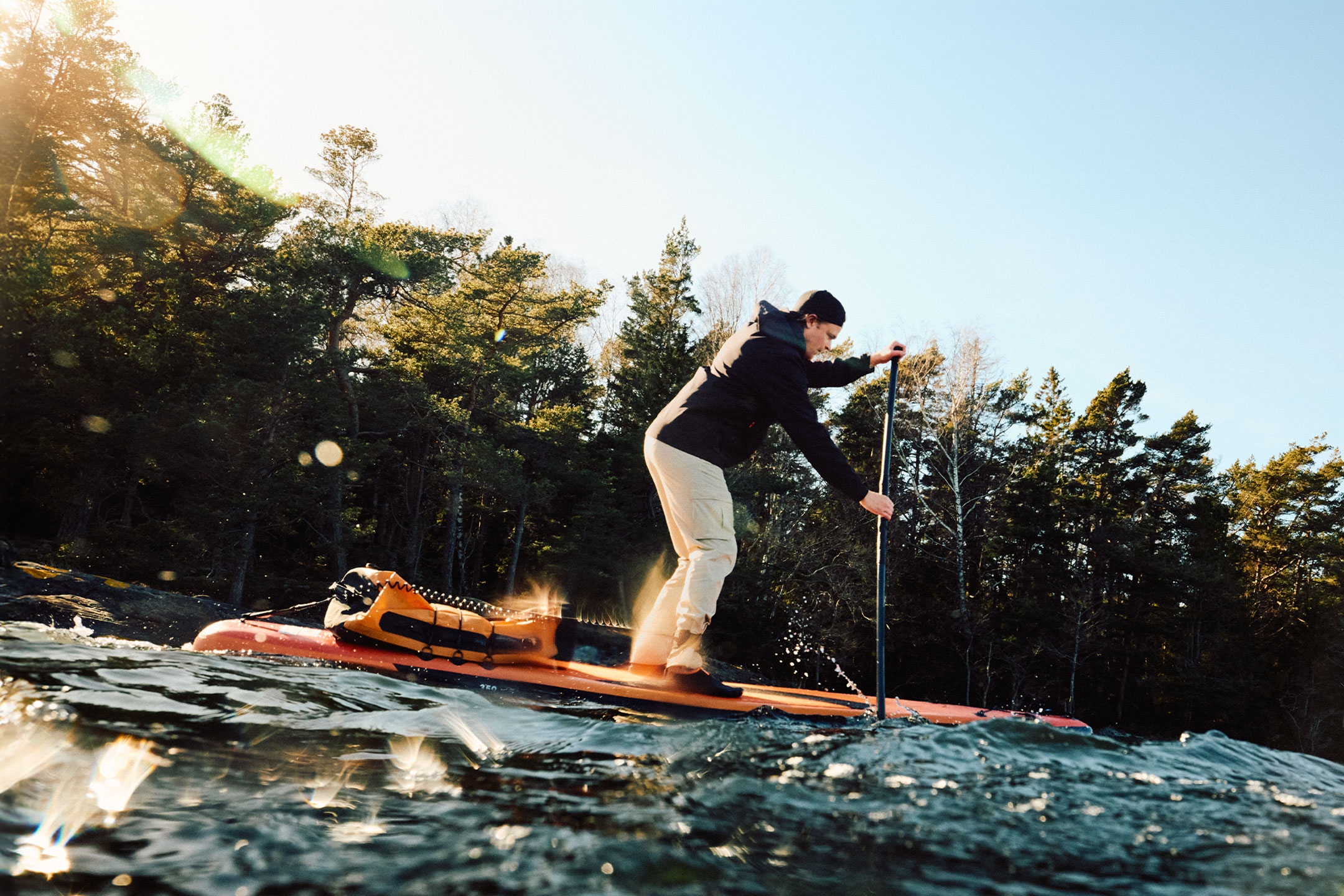 Mand i beige bukser og sort jakke padler på et orange paddleboard