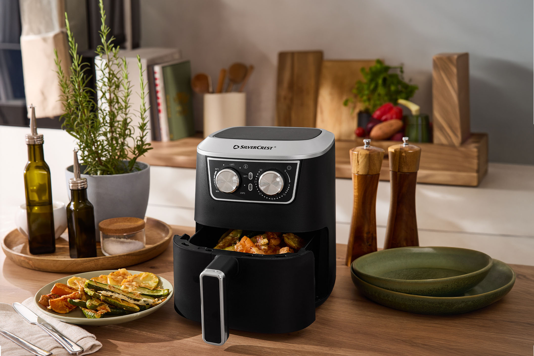 Airfryer med ristede grøntsager, olivenolie, salt og peber på køkkenbordet.