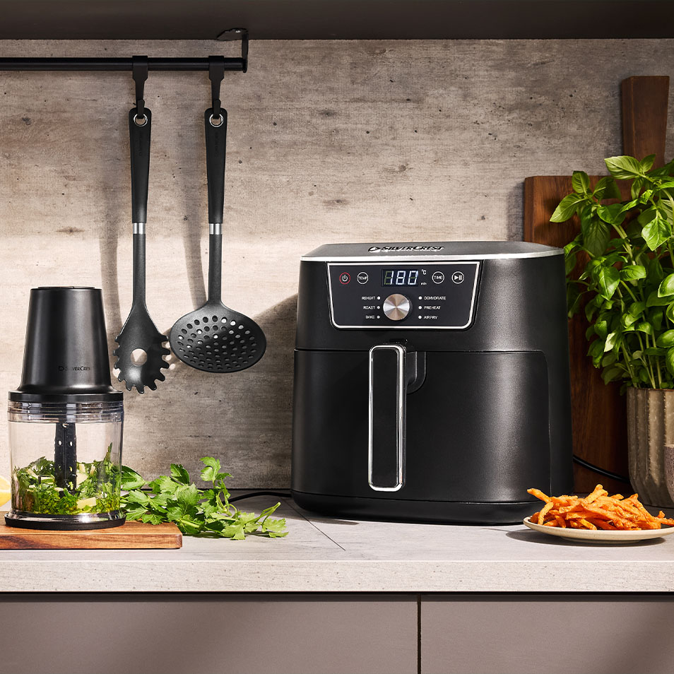 SilverCrest airfryer og foodprocessor på køkkenbord med friske krydderurter og søde kartoffelpomfritter.