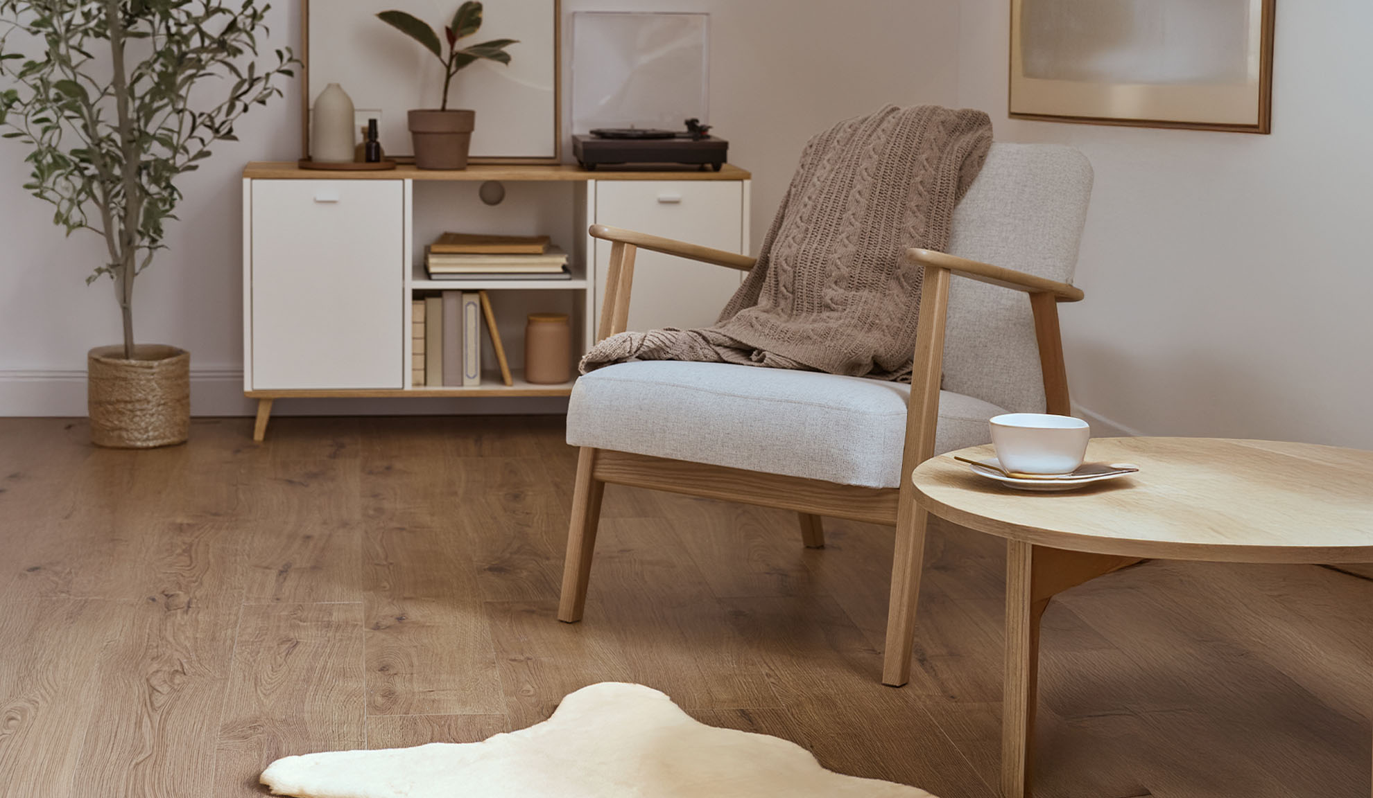 Hyggelig lænestol med tæppe, træsofabord og opbevaringsskab i en lys stue.