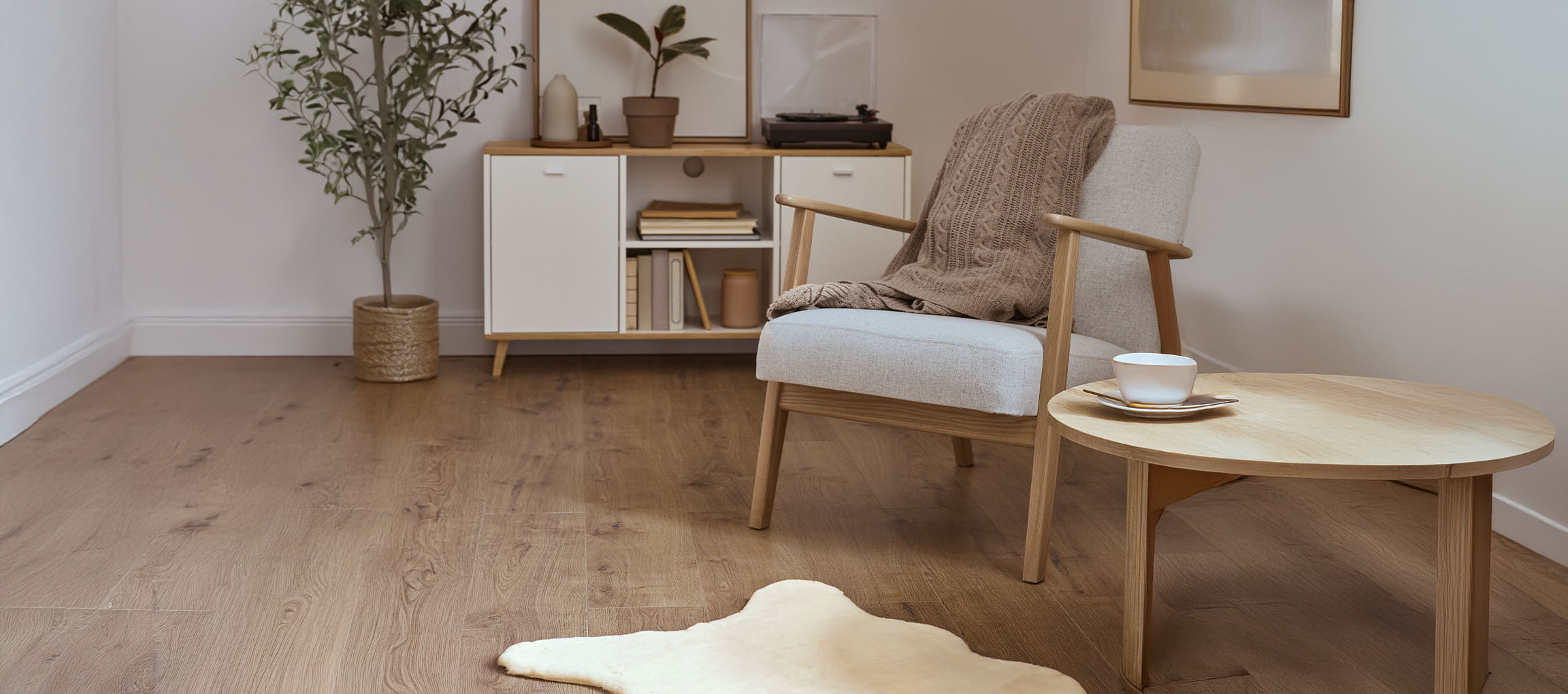 Grå stoflænestol med strikket tæppe, træsofabord og moderne skænk.