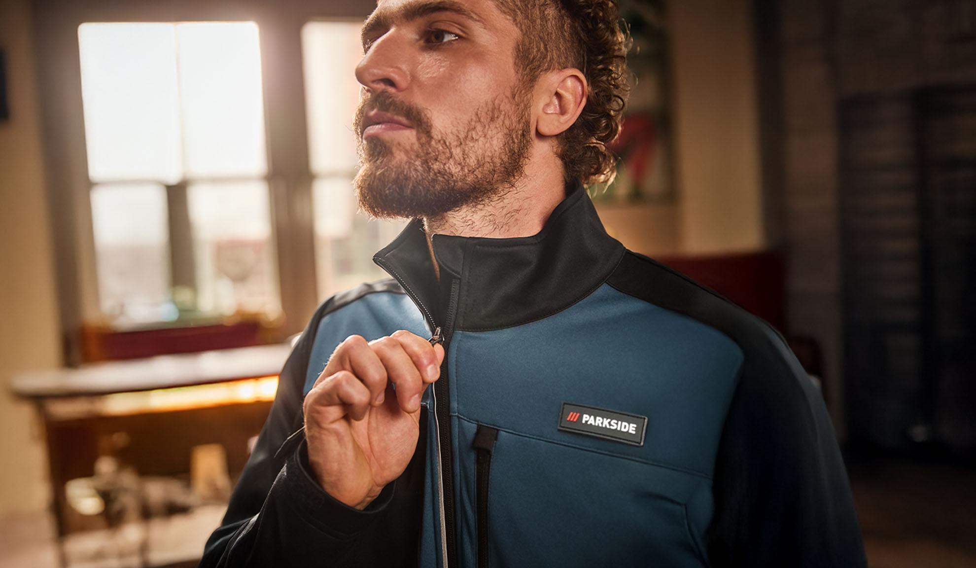 Mand i en blå og sort Parkside arbejdsjakke, der lyner den op.