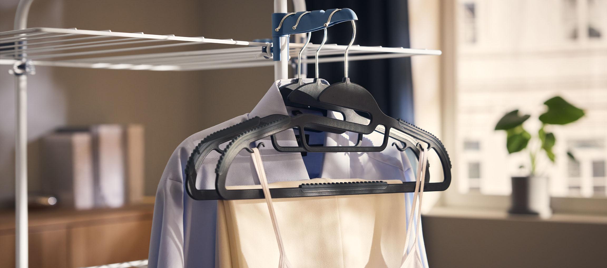 Tøj på bøjler på et tørrestativ, med en plante i baggrunden.