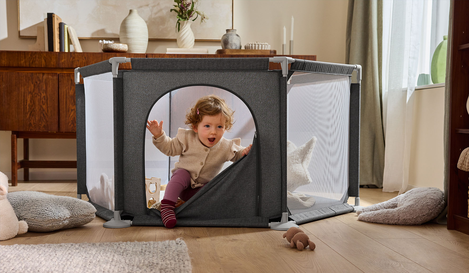 Glad baby kravler ud af en grå kravlegård i en hyggelig stue.