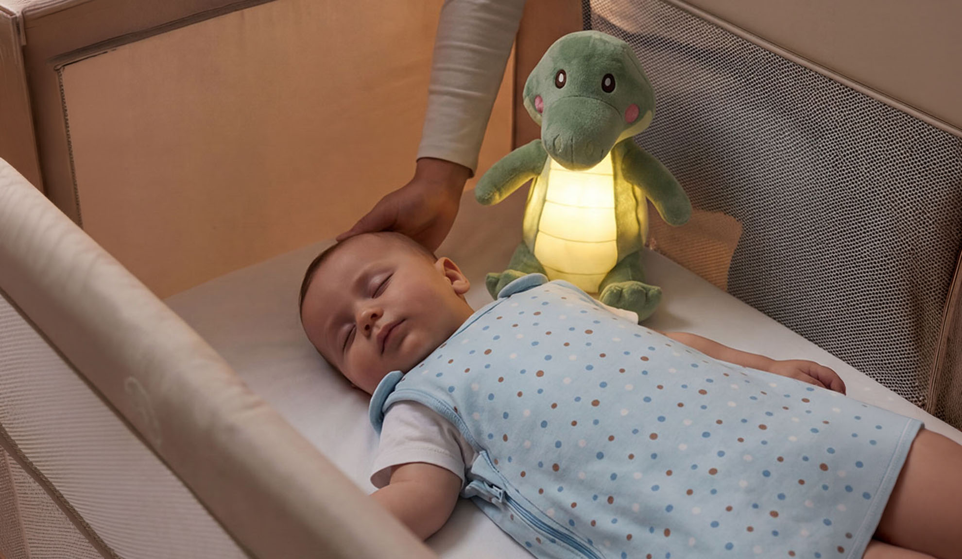 Baby sover i tremmeseng med blødt legetøj og forældres hånd.