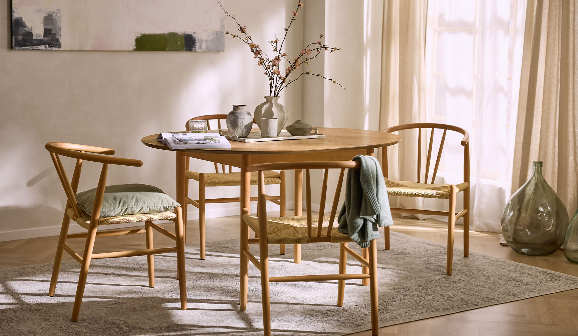 Lyst spiseområde med rundt træbord, træstole med flettede sæder og blomsterdekoration.