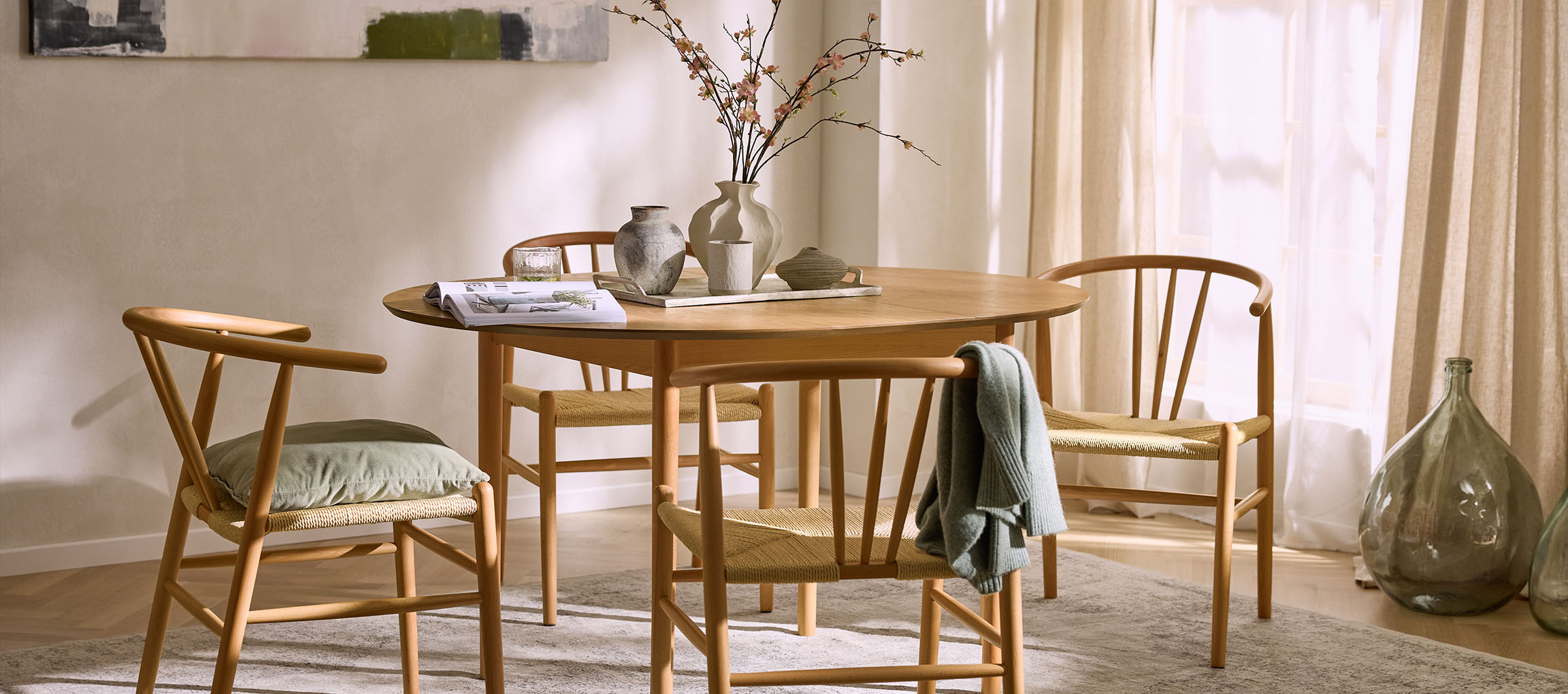 Spisestue med rundt træbord, træstole med flettede sæder og dekorative vaser.