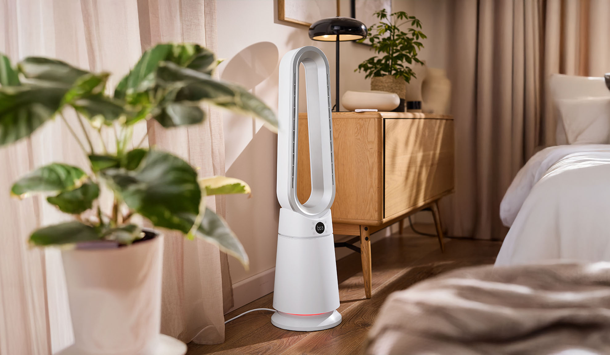 Hvid tårnventilator i et moderne soveværelse med planter og træmøbler.