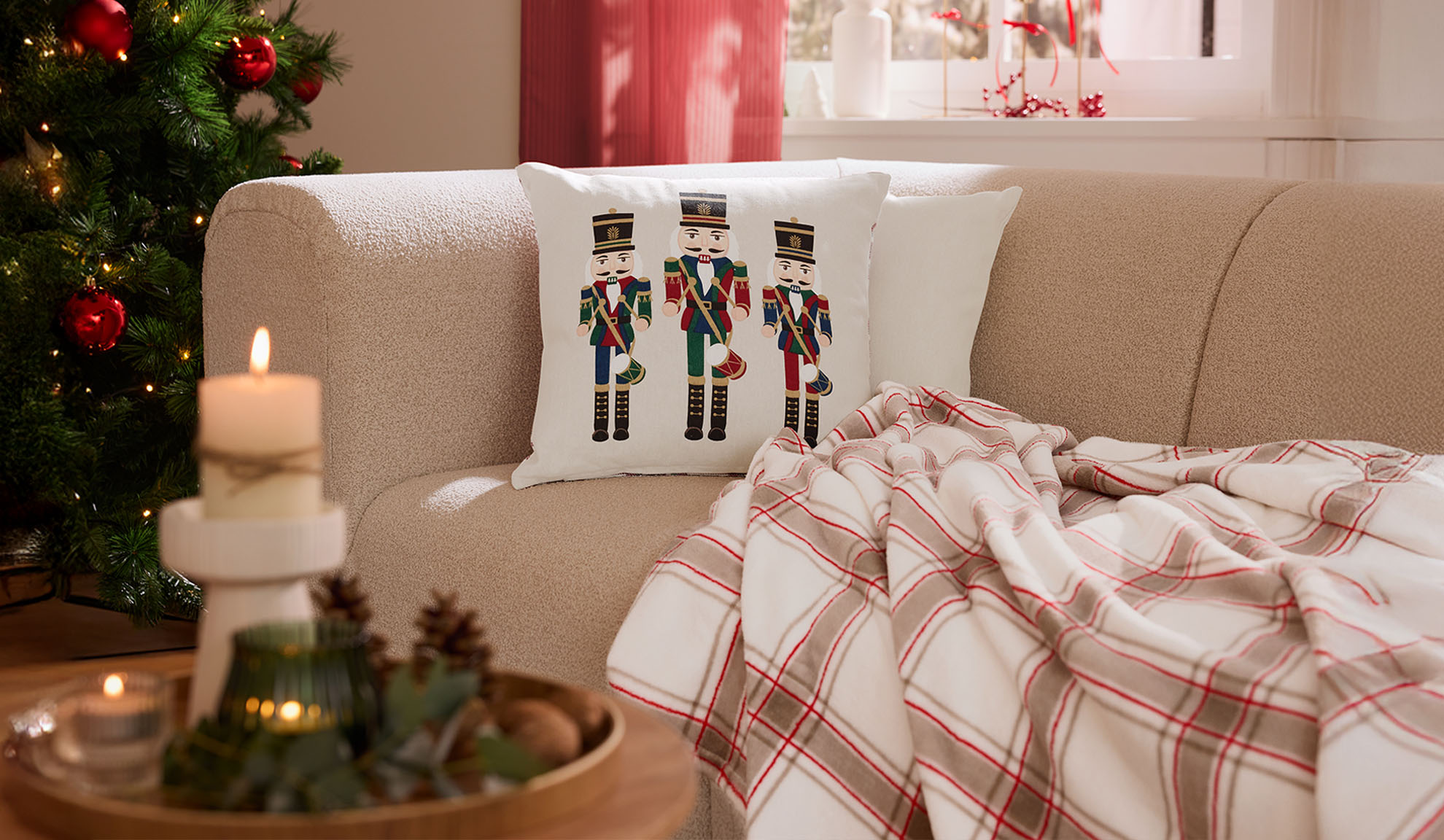 Julestue med sofa, nøddeknækkerpuder, ternet plaid og stearinlys.