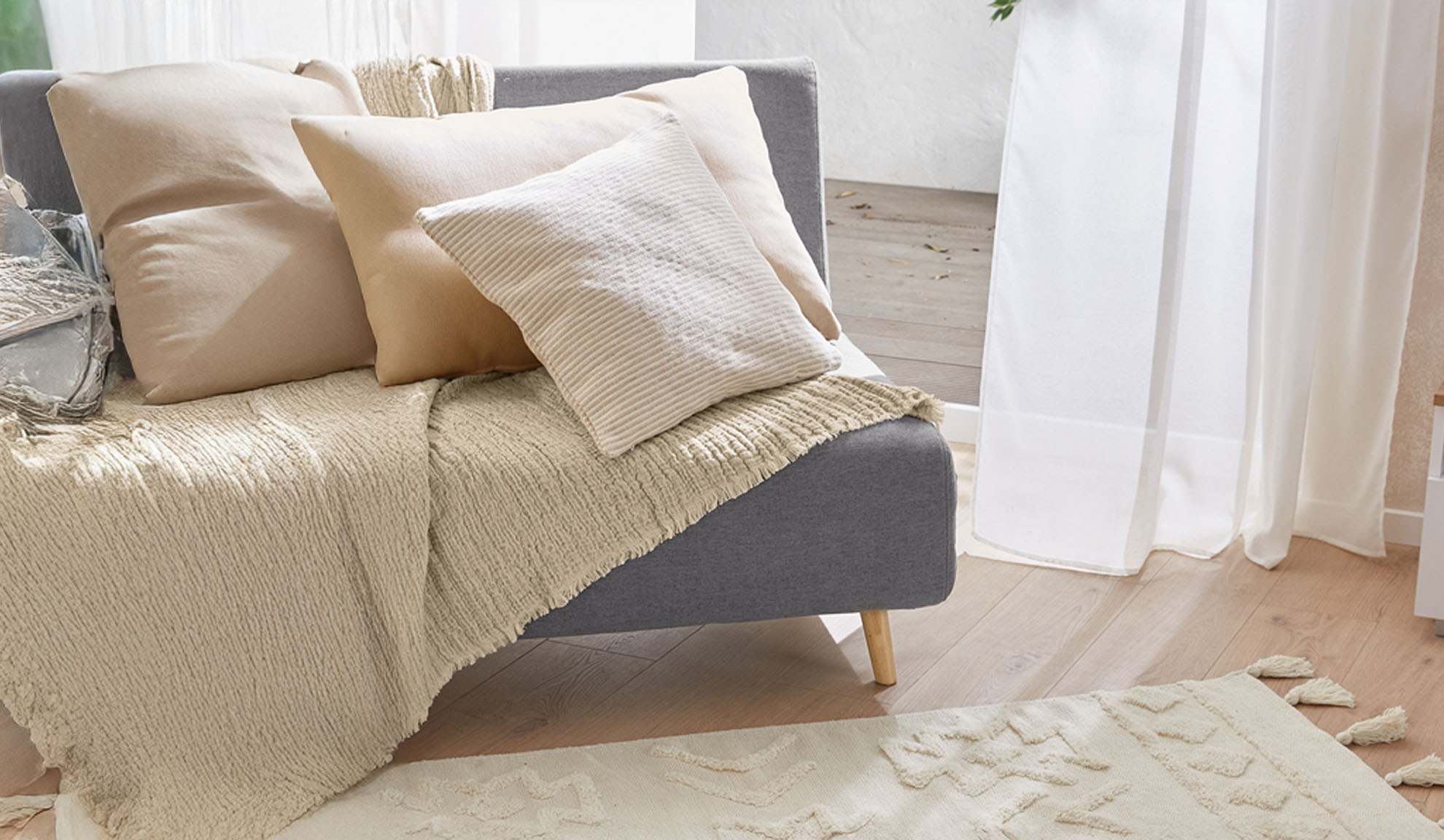Grå sofa med beige puder og tekstureret tæppe i en lys stue.