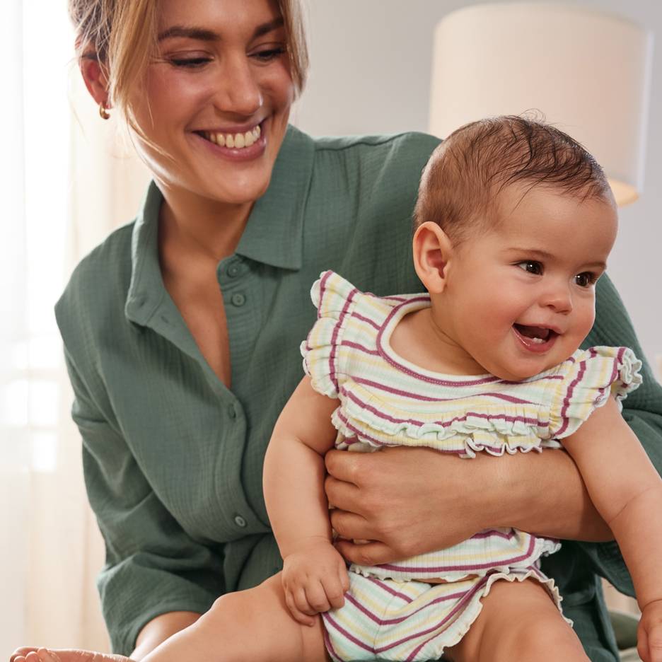 Smilende mor med glad baby i farverigt stribet sæt.