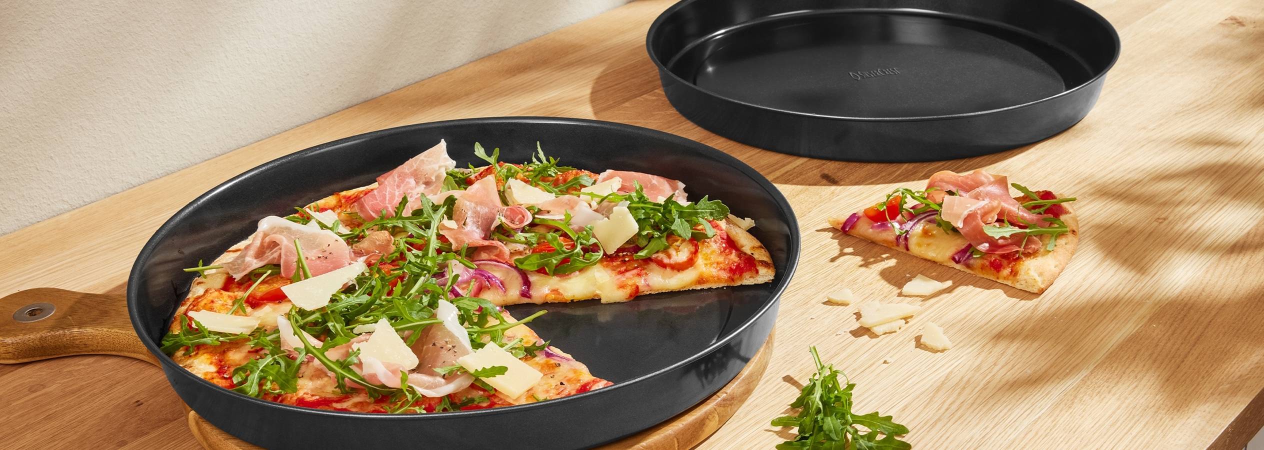 Pizza med skinke, rucola og ost i en sort pizzapande på et træbord.