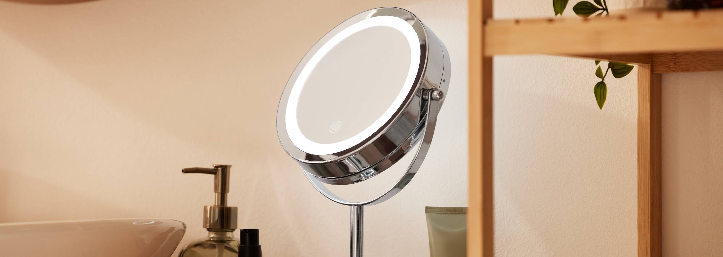 Et elegant, LED-oplyst spejl med drejelig arm står på et badeværelsesbord.