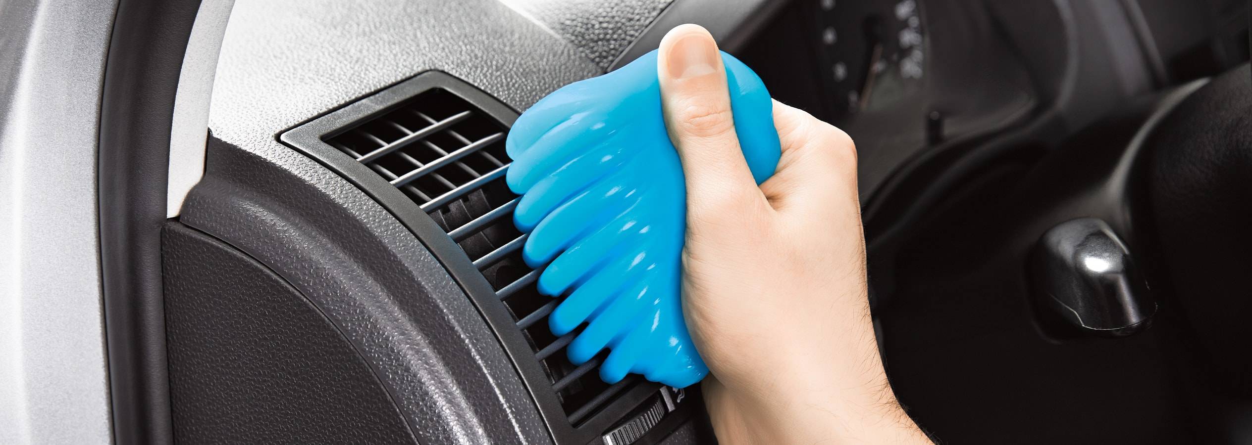 En hånd bruger blå rengøringsgel til at rengøre bilens ventilationsåbninger.