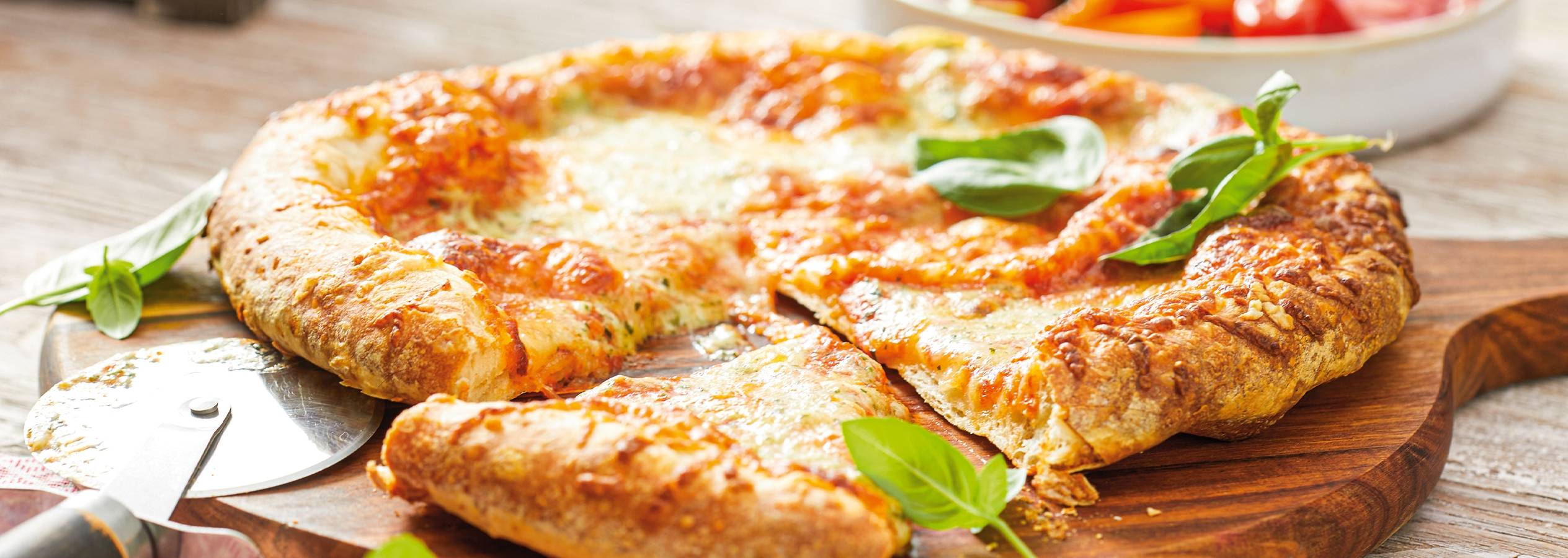 En lækker, sprød pizza med ost og basilikum på et træbræt.